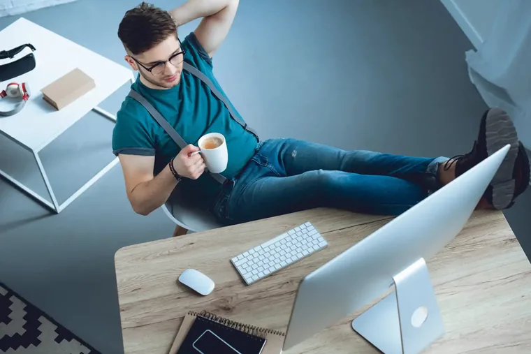 A builder leaning back from a desktop with a coffee, mid-project